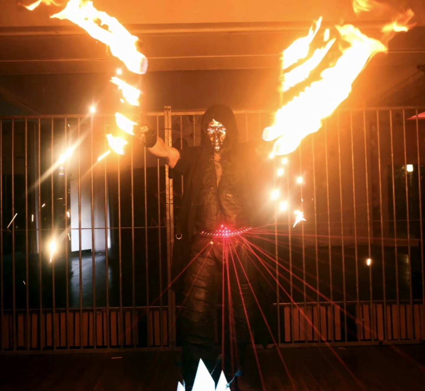 Mike Garcia masqué, bras ouverts, flammes et faisceaux lasers rouges